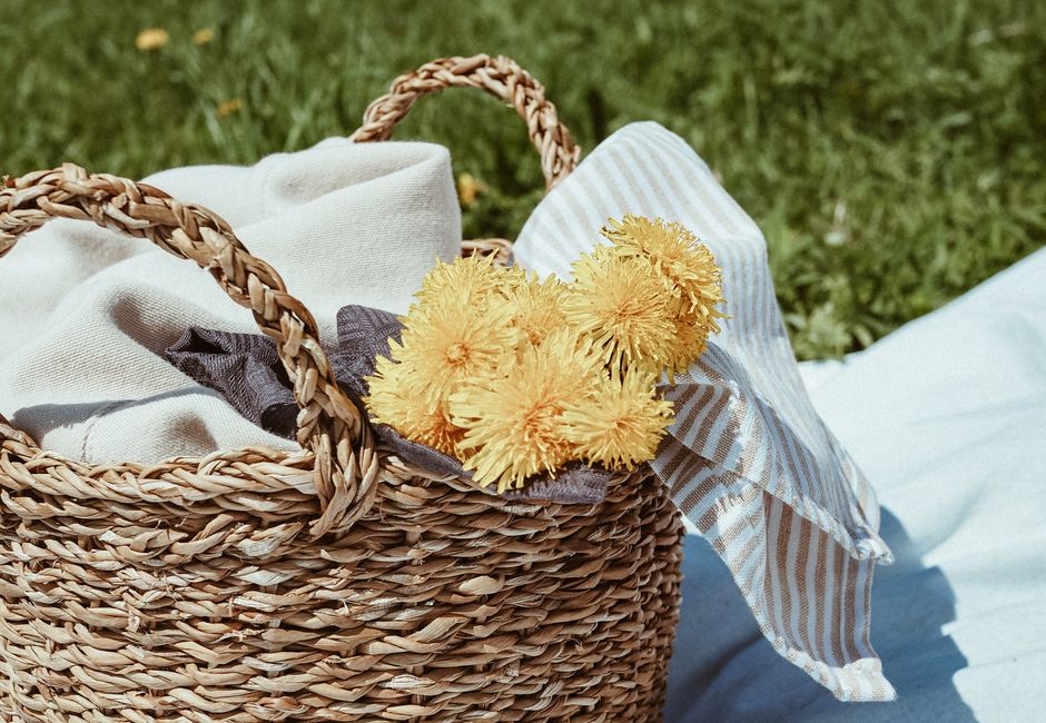 Close-up of a wicker basket with yellow dandelions outdoors on a sunny day.